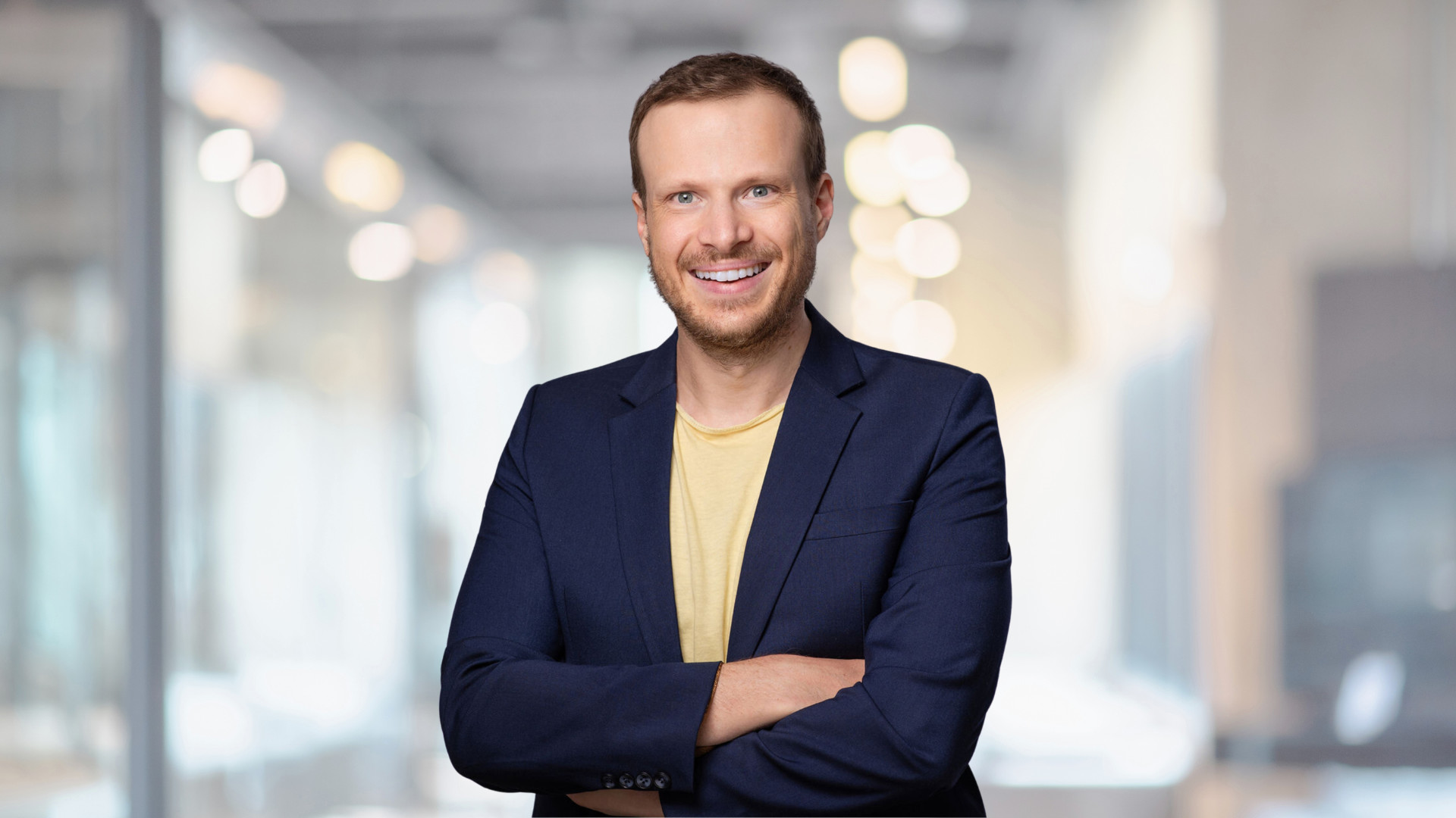 Business-Porträt von Damian Holmer mit verschränkten Armen in modernem Unternehmensumfeld